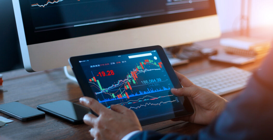 Businessman checking stock market on digital tablet and a desktop computer with stock exchange graph on screen. Financial stock market. Analyzing data in office background.